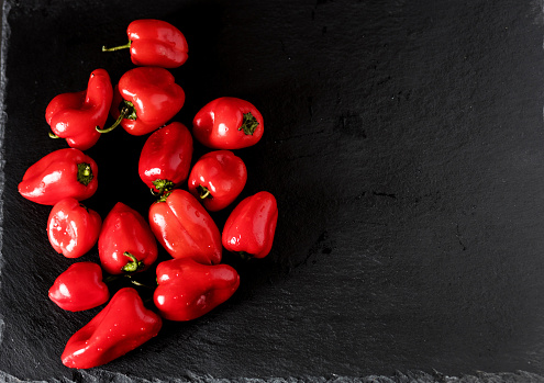 Raw organic mini sweet red peppers on black board. copy space