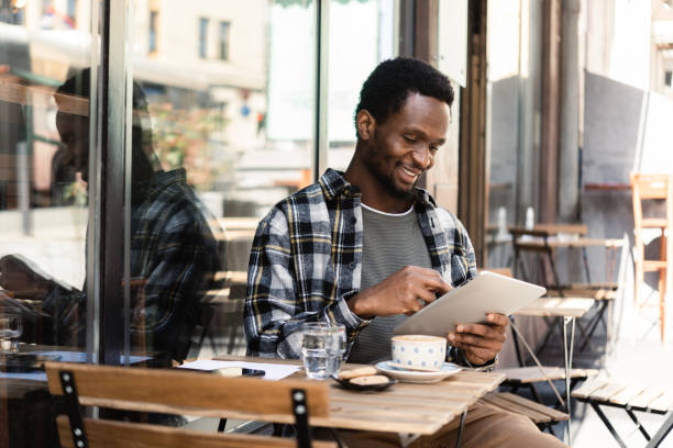 istock Happy African young man enjoying coffee at the cafe and using digital tablet 1413585937