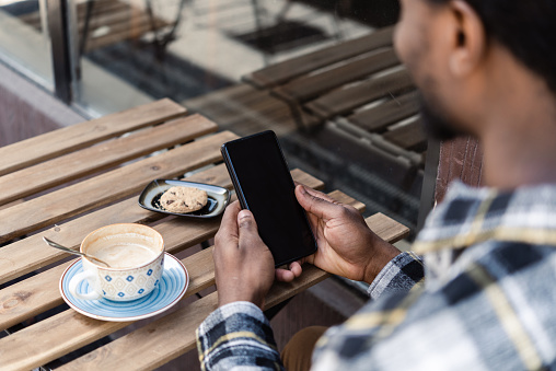 Young African American man using smartphone and enjoying coffee in the city