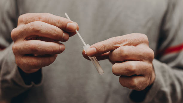 istock hands introducing nasal swab of covid antigen test into liquid in foreground 1413586956
