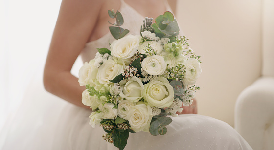 Beautiful, colorful and fresh wedding flowers for a woman on her special day. Closeup of a bride holding a bouquet of roses against her white dress while getting ready for a celebration or event
