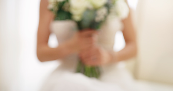 Beautiful, fresh flowers and a woman on her wedding day. Bride holding a bouquet against her white dress while getting ready for her marriage celebration as a bokeh or blurred background