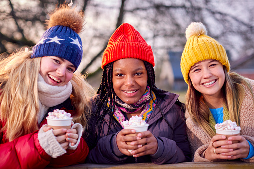 Portrait Of Teenage Girls Enjoying Hot Chocolate On Snowy Winter Walk In Countryside Together