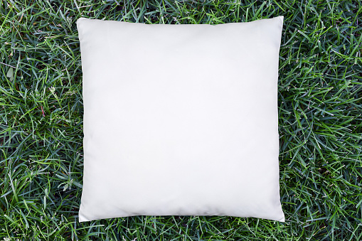 White pillow cushion enjoying a spring day atop a lush green lawn.