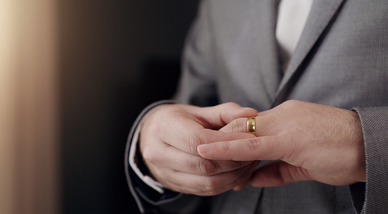 Man touching or taking wedding ring off finger with hand and thinking, feeling sad and angry. Closeup of depressed or frustrated groom feeling lonely, upset or worried over cheating or affair scandal