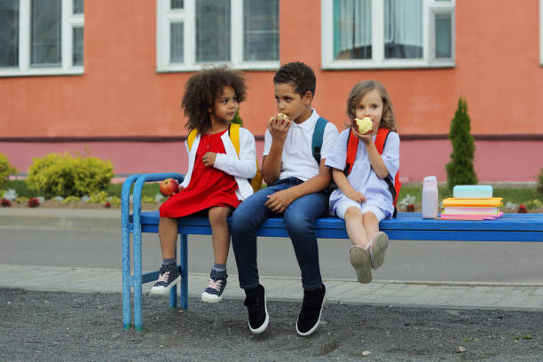 lindos escolares negros y niñas están comiendo al aire libre al lado de la escuela. - apple healthy eating eating black fotografías e imágenes de stock