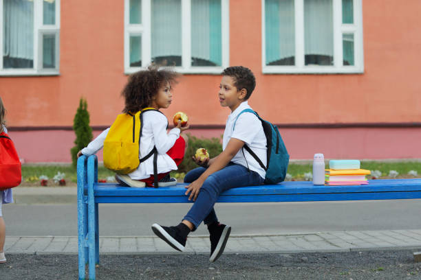 Cute Black schoolboy and girl are eating outdoors next the school. Cute Black schoolboy and girl eating outdoors next the school. Healthy school breakfast for child. Food for lunch, lunchboxes with sandwiches, fruits, vegetables, and water. food elementary student healthy eating schoolboy stock pictures, royalty-free photos & images