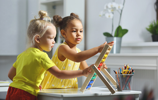 White and Black children sit together at the table and count on the abacus and smiles. Math lesson in elementary school