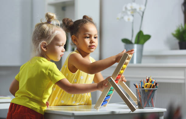 children of different races sit together at the table and count on the abacus White and Black children sit together at the table and count on the abacus and smiles. Math lesson in elementary school checking the time stock pictures, royalty-free photos & images