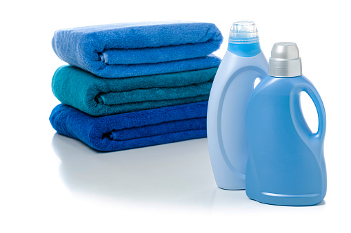 Front wiew of two blue plastic bottles of fabric softener and detergent isolated on white background. A stack of blue towels complete the composition. High resolution 42Mp studio digital capture taken with Sony A7rII and Sony FE 90mm f2.8 macro G OSS lens