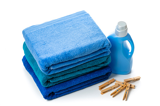 High angle wiew of a blue plastic bottle of fabric softener or detergent isolated on white background. A stack of blue towels and clothes pins complete the composition. High resolution 42Mp studio digital capture taken with Sony A7rII and Sony FE 90mm f2.8 macro G OSS lens