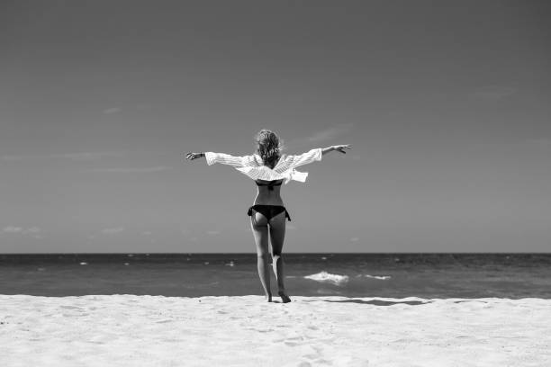 single happy young woman in swimsuit and white blouse at sand sea beach with clean sky