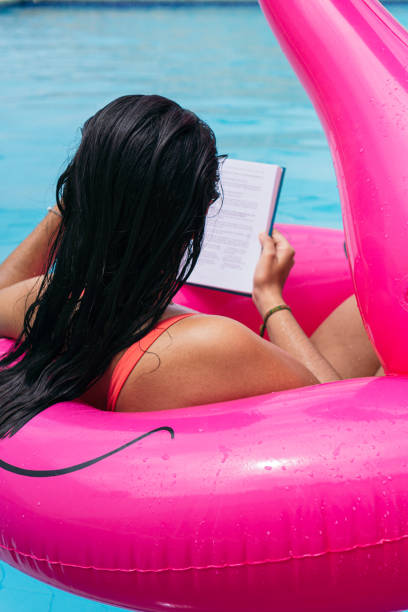 istock Woman sitting on an inflatable reading a book at the pool 1413594831