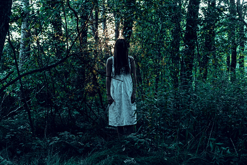 Scary woman standing in forest. Halloween theme.