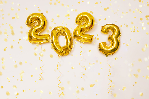 Gold 2022 balloons on a white wall background with confetti and lights. New Years celebration concept