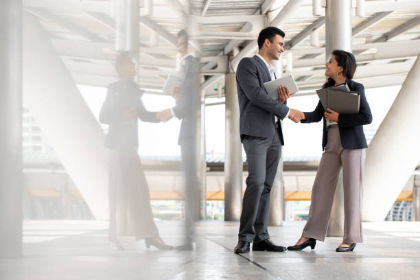 hombre de negocios indio saludando y haciendo apretón de manos con una mujer de negocios al aire libre en la pasarela de la ciudad - men women handshake business fotografías e imágenes de stock