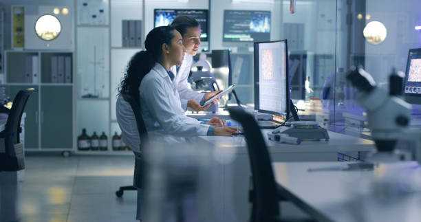 Focused, serious medical scientists analyzing research scans on a computer, working late in the laboratory. Lab workers examine and talk about results from a checkup while working overtime Medical researchers looking at and examining a brain scan on a computer while working late in an office together. Lab workers analyzing and talking about results from a checkup while working overtime medical clinic stock pictures, royalty-free photos & images