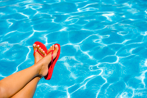 Close up of woman foot with red flip flops by the pool.
