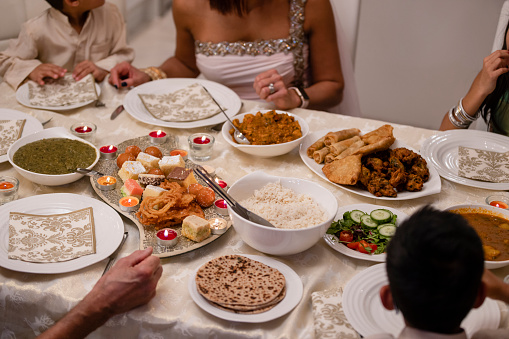 A high angle view of a dinner table which is laid out with lots of tradiotional fresh food that they are going to eat  to celebrate Diwali as a family in their home in the orth East of England. There is Jalebi, Samosas, Bhajis, Aloo Chaat, Saag Aloo and Curry
