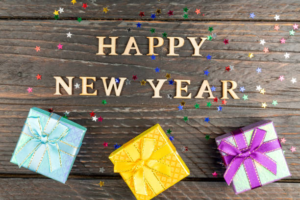 istock Multicolored gift boxes with tied bows. New year presents on wooden table with scattered confetti stars. Text Happy new year. Festive greeting card. Flat lay. 1413603228