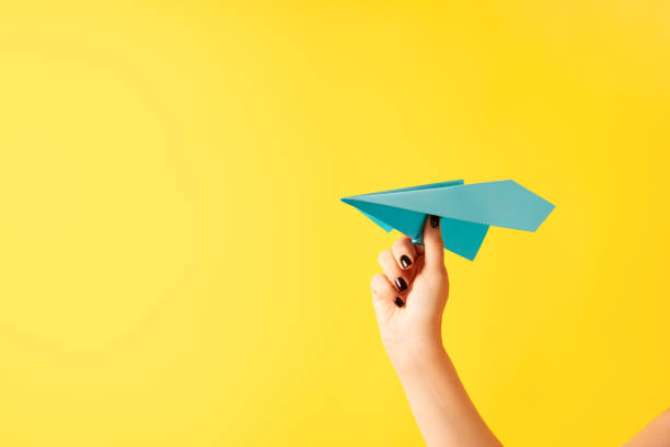 istock A woman's hand holds blue paper airplane on yellow background 1413605877