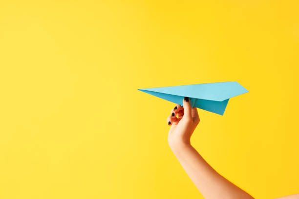 istock A woman's hand holds blue paper airplane on yellow background 1413605878