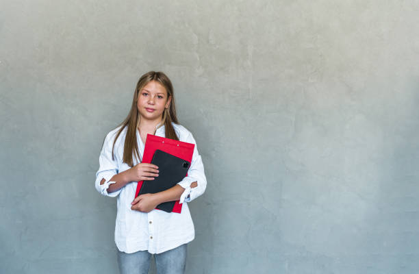 istock Happy young female student holding notebooks from courses and smiling at camera, standing in spring clothes against blue 1413606398
