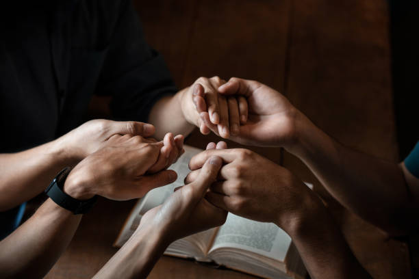 um grupo de jovens cristãos de mãos dadas em oração pela fé e escrituras em uma mesa de madeira enquanto rezam a deus. - bible church studying group of people - fotografias e filmes do acervo