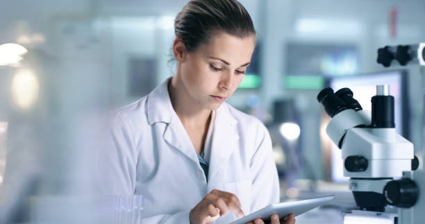 istock Serious female scientist recording virus cell data onto online database with a tablet while working inside a lab or research center. Focused researcher reading medical journal in a health care center 1413607269