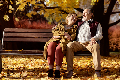 Shot of a senior Caucasian couple enjoying coffee while sitting on a bench next to a lake in a public park. Smiling and  enjoying life.