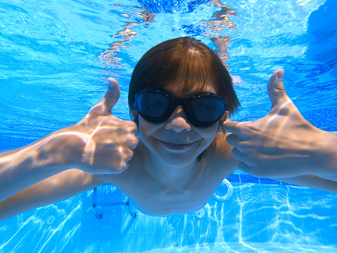 Little boy aged 10 swimming underwater. The boy is smiling at the camera showing thumbs up.