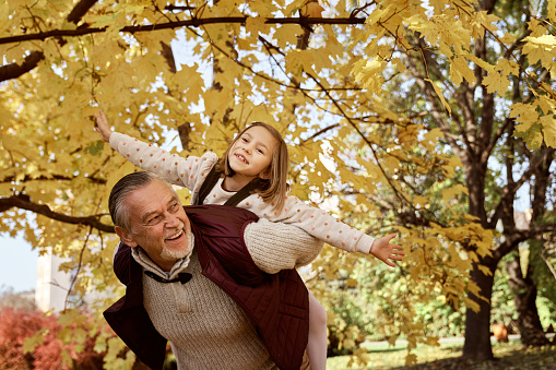 Senior man with her granddaughter playing at the park in the autumn