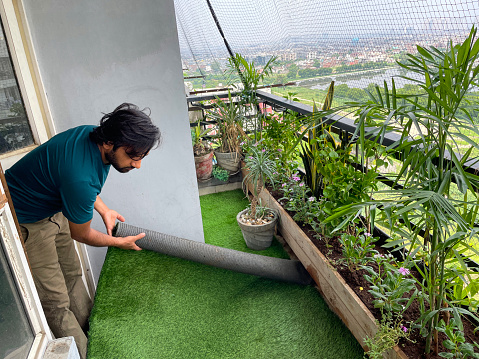 Stock photo of apartment balcony in Ghaziabad, India decorated with wooden raised beds, potted plants and artificial green grass turf. Low maintenance gardening and exterior design concept.