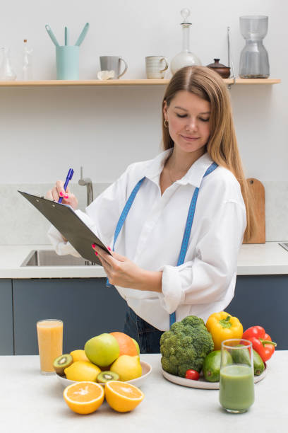 istock A young nutritionist woman makes a nutrition plan in her form while standing near a table with fresh vegetables, fruits 1413614116