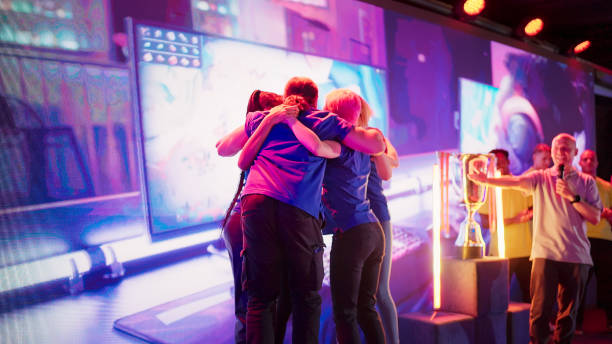 esport commentator introducing competing teams with african ethnicity players at video game championship. blue team in group hug - esport audience bildbanksfoton och bilder