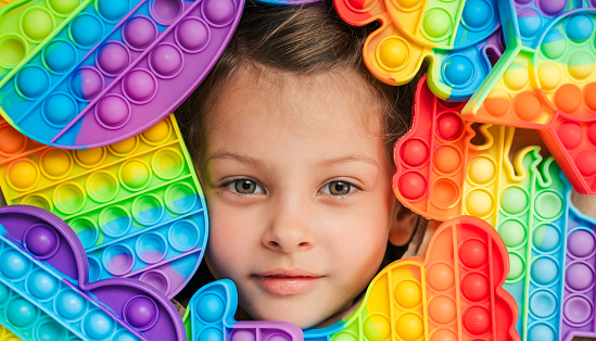 Little girl,kid,child head among many,lots of colorful pop it. Children play. Trendy silicone antistress colorful sensory push toy popit. Flapping fidget. Rainbow color.Cure of autism.Stress reliever.