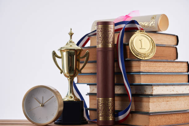 gold medal ,trophy , clock ,stack of books and certificate against white background