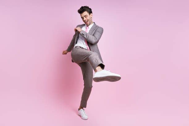 istock Happy young man in full suit throwing leg kick while standing against pink background 1413625323