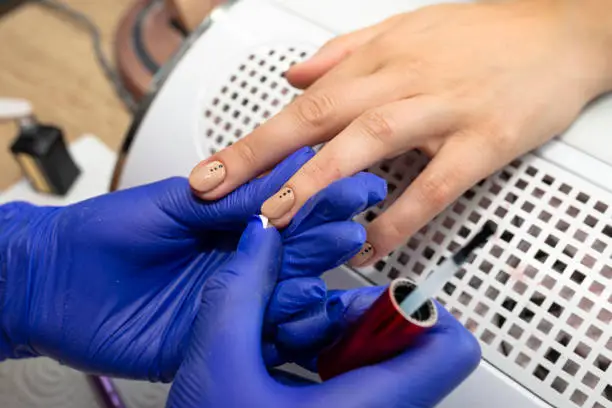 Photo of The manicurist applies a topcoat to the finished hybrid nails with a brush.
