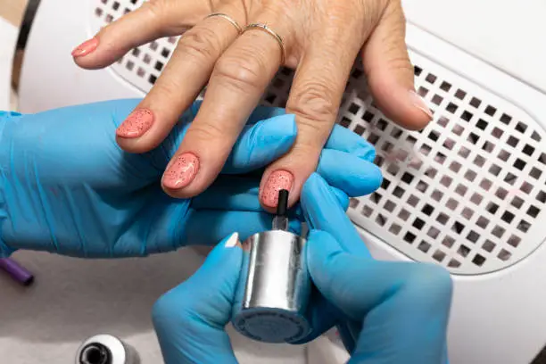 Photo of The manicurist applies a topcoat with black dots to the finished hybrid nails with a brush.