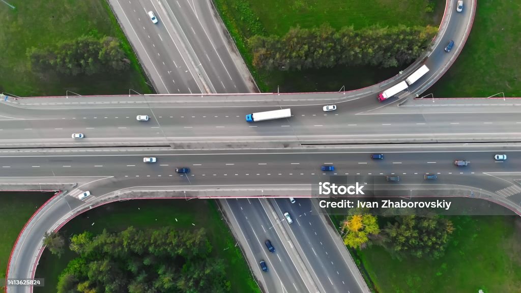 The drone flies over the track during traffic with many interchanges in different directions with a large number of cars that move one after another and change lanes to the desired exit from the track Highway Stock Photo