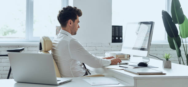 istock Concentrated man in shirt and tie using computer while sitting at his working place in office 1413625874
