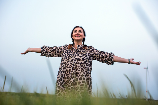 beautiful woman in her fifties standing outdoors in a field spreading her arms