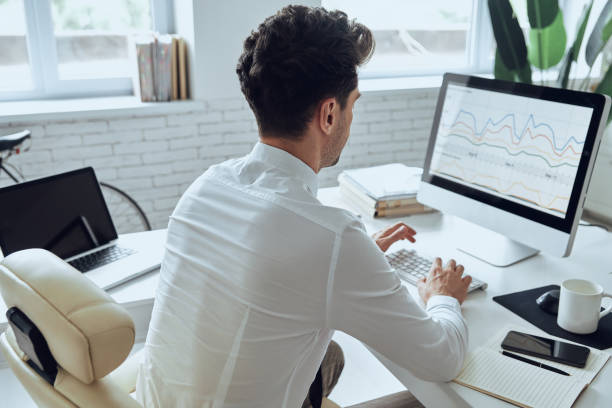 istock Rear view of man using computer while sitting at his working place in office 1413629188