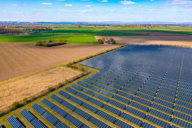 A drone view of a solar park with photovoltaic panels next to fields and a farm