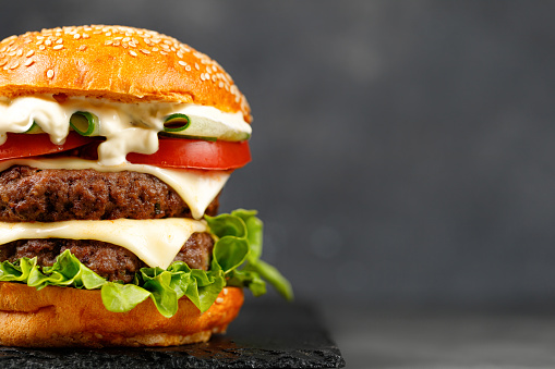 Close up Burger with beef cutlets, Cheese, cucumber, lettuce on black background. Fast Food Restaurant menu