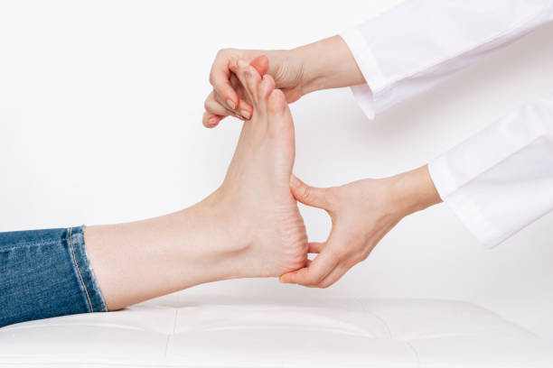 Examination of a young woman by an female orthopedist. Cropped shot of doctor holding a painful foot Examination of a young woman by an female orthopedist. Cropped shot of doctor in a white coat holding a painful foot in her hands. Flat feet, injury. Foot treatment. Pain from uncomfortable shoes pes planus stock pictures, royalty-free photos & images