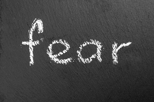 Grunge word FEAR written in chalk on a black rough slate chalkboard close-up. Halloween horror concept