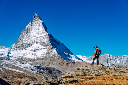 Young Caucasian man walking in nature near Matterhorn mountain in Switzerland alpine hiking\nman taking a picture with phone