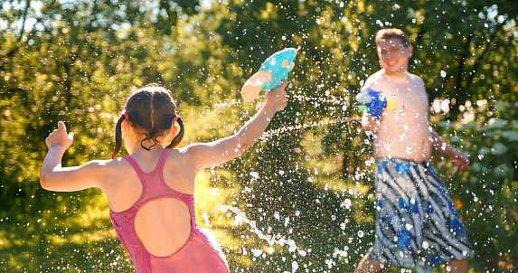 Little girl in swimwear, daughter dad, daddy, father swim, play water pistols, guns in children's inflatable pool in backyard of country house. Summer funny family outdoor games,recreation.Staycation.